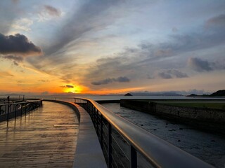 Coastal landscape with a pier under a cloudy sunset sky