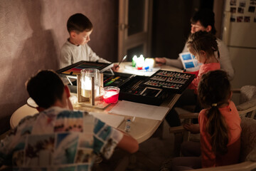 Family spending time together during an energy crisis in Europe causing blackouts. Kids drawing in blackout.