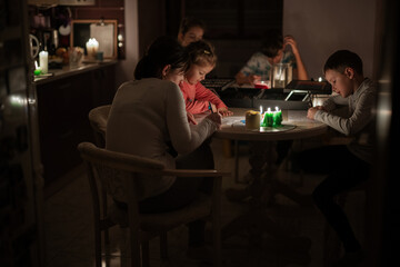 Family spending time together during an energy crisis in Europe causing blackouts. Kids drawing in...