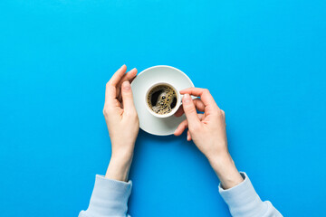 Minimalistic style woman hand holding a cup of coffee on Colored background. Flat lay, top view cappuccino cup. Empty place for text, copy space. Coffee addiction. Top view, flat lay