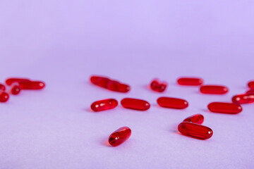 Heap of red pills on colored background. Tablets scattered on a table. Pile of red soft gelatin capsule. Vitamins and dietary supplements concept