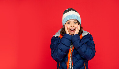 winter fashion. surprised kid with curly hair in puffer jacket and hat. teen girl on red background.