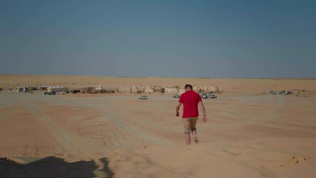 Man back heading to the Star Wars background scenery of famous movie Star Wars. Tourist person walking towards movie decoration in sahara..