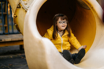 Happy child with down syndrome enjoying swing on playground