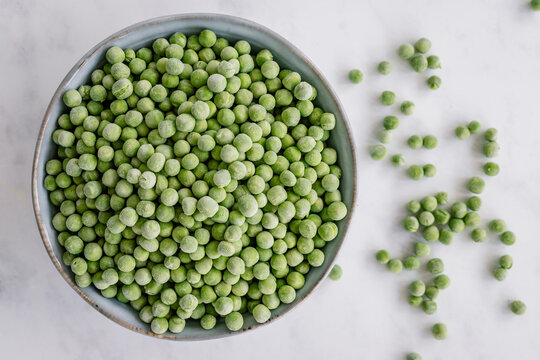 Overhead view of a bowl of frozen green peas on a table