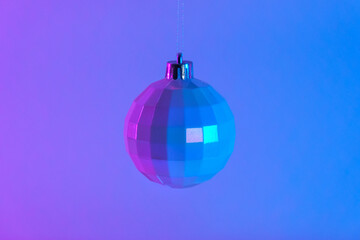 Fototapeta premium Christmas white ball in neon light. New Year 2023. The ball is hanging on a blue pink background. The postcard is in purple. Merry Christmas. Minimalism.