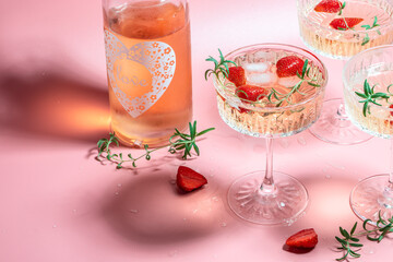 Boozy Refreshing Rose Wine, strawberry cocktail or mocktail, refreshing summer drink with champagne, strawberries, ice cubes and rosemary on pink background