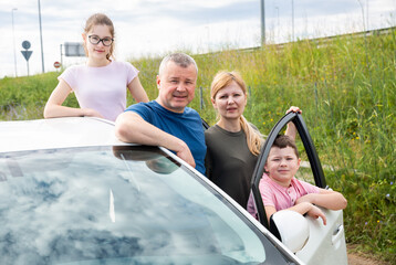 Happy family of four posing next to new purchased car