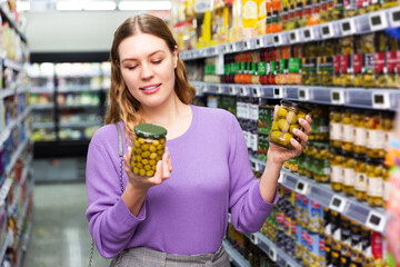 Smiling young woman readig label on jar of preserved olives in the shop