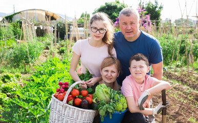 Portrait of happy parental couple with teen daughter and preteen son posing with fresh harvest in backyard garden.