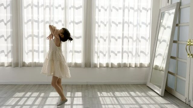 Portrait of little asian child girl dreams of becoming ballerina in a pink tutu skirt in morning light white studio. Happy young girl practise her dance. Education childhood toddler lifestyle concept