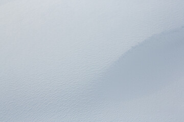 Beautiful winter background with snowy ground. Natural snow texture. Wind sculpted patterns on snow surface. Closeup top view with copy space.