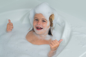 Kids face in foam. Kid washing with a bubbles in bath. Cute child bathes, lying in a white bath...