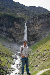 Naklejka premium Traveler guy standing wearing shirt with sleeves roll up and beautiful massive glacier melt water waterfall in background