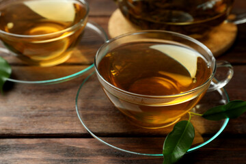 Fresh green tea in glass cups with saucers and leaves on wooden table, closeup