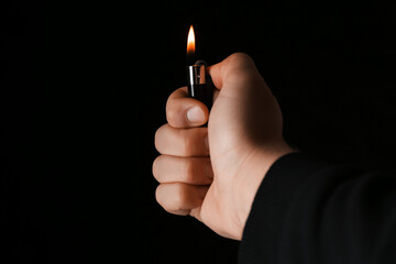 Man holding lighter on black background, closeup - obrazy, fototapety, plakaty