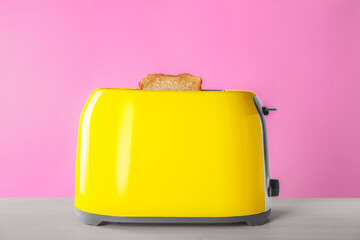 Modern toaster with slices of roasted bread on white wooden table