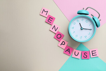 Pink paper notes with word Menopause and alarm clock on color background, flat lay. Space for text