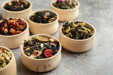 Different kinds of dry herbal tea in wooden bowls on light grey table