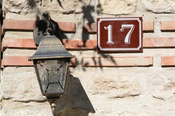 Plate with house number seventeen near lantern on stone wall outdoors