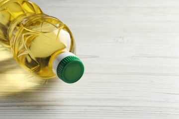 Plastic bottle of cooking oil on white wooden table, space for text