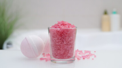 Glass with sea salt and bath bombs on table in bathroom, closeup
