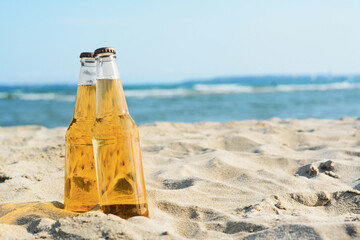 Bottles of cold beer on sandy beach near sea, space for text - obrazy, fototapety, plakaty
