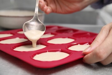 Woman pouring batter into baking mold at table, closeup. Madeleine cookies