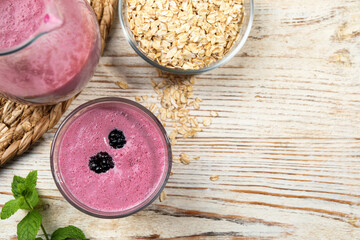 Glass of blackberry smoothie with mint and oatmeal on light wooden table, flat lay. Space for text