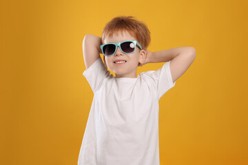 Cute little boy with sunglasses on yellow background