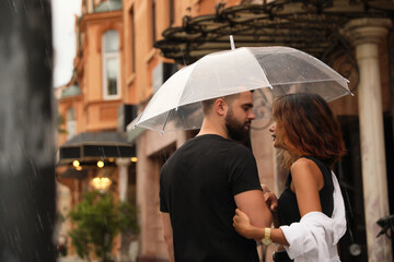 Young couple with umbrella enjoying time together under rain on city street