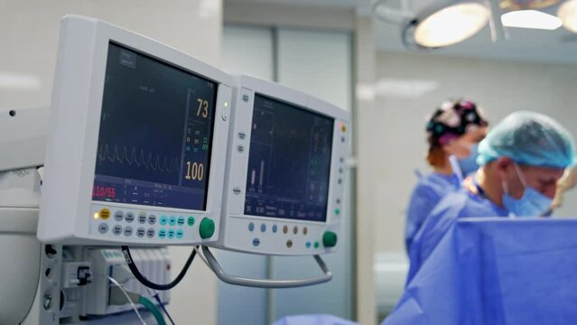 Modern equipment for lung ventilation at operational theatre. Couple of screens at apparatus working during surgery. Doctors performing operation at backdrop in blur.