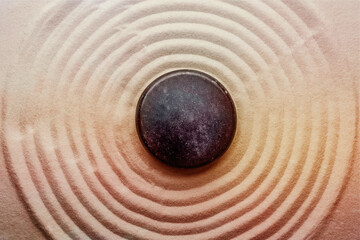Fototapeta na wymiar Black stone on sand with pattern, top view. Zen, meditation, harmony
