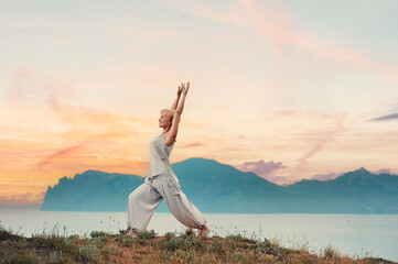 Senior woman doing yoga exercises with mountain sunset on the background