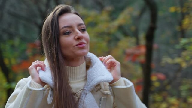 Nice-looking Caucasian lady puts her jacket collar up. Smiling relaxed woman walking in the nature on autumn day.