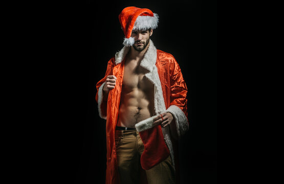 Christmas sexy man. Strong guy in santa hat. New year strip and gifts for adults. Muscle gay at xmas. Santa with muscular body. Sexy young Santa Claus on black background.
