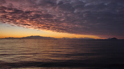 Pink clouds in an orange sky, with mountains and icebergs in silhouette, at Cierva Cove, Antarctica, at sunset