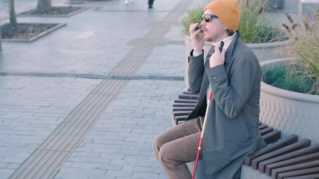 Visually Impaired Man Talking On The Phone, Sitting On The Bench In The City.