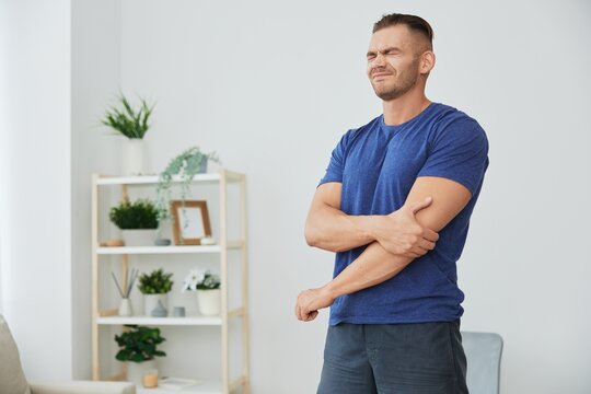 A man has pain in his arm, sprain of muscles and ligaments during sports, inflammation and injury, in a blue t-shirt at home