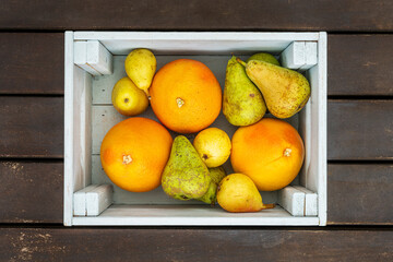 A wooden box full of ripe citrus and assorted pears