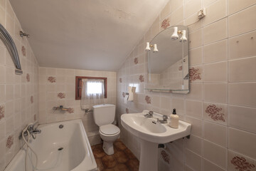 Bathroom with patterned tiles and white porcelain toilets, matching bathtub and wooden window with white curtains