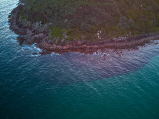 Drone photo looking down at the coastline of Shark Island, Fingal Bay, with contrasting shallow and deep blue water.