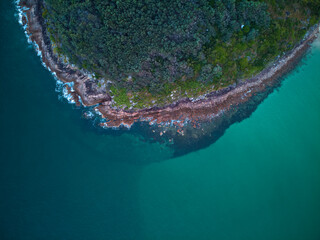Drone photo looking down at the coastline of Shark Island, Fingal Bay, with contrasting shallow and deep blue water.