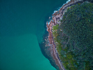 Drone photo looking down at the coastline of Shark Island, Fingal Bay, with contrasting shallow and deep blue water.