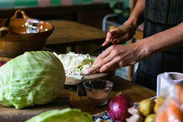 Hands of an unrecognizable person chopping cabbage in a rustic kitchen. Food.