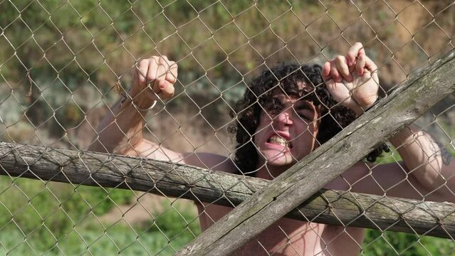captivity, despair - young man locked up behind a net screams desperately