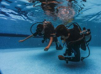diving instructor teaches students to scuba dive in swimming pool. couple getting first experience with scuba diving under the guidance of experienced recreational diving instructor on vacation.