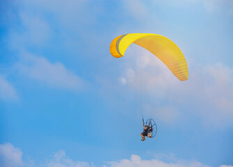 A yellow paraglider with a paramotor, soaring in the rays of the evening sun.