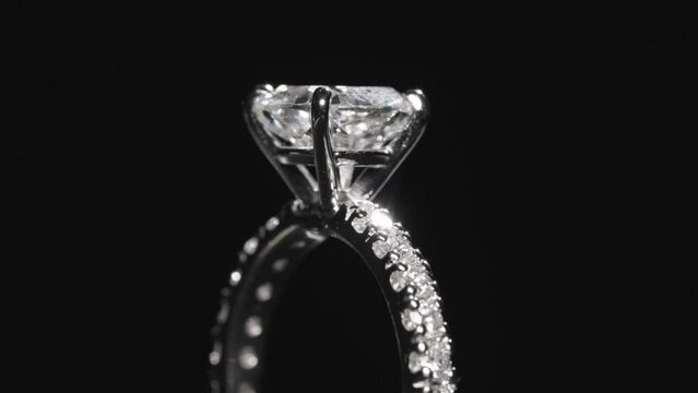 Close up, diamond engagement ring rotating against black studio background