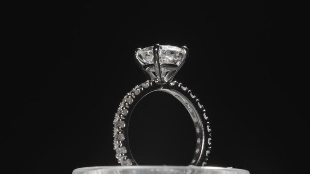 Beautiful diamond engagement ring rotating, reflecting light. Back studio background